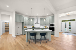 Open-concept kitchen with a large white island, light gray cabinets, and pendant lights above.