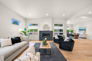 Open-concept living room with a central fireplace, round mirror above, light furniture, and a dining area in the background.