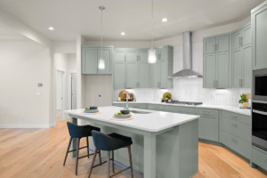Modern kitchen with mint-green cabinets, a large white island, pendant lights, and stainless steel range hood over a gas stove.
