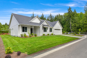 White modern single-family home with a manicured lawn, front porch, and a two-car garage, set against trees and a blue sky.