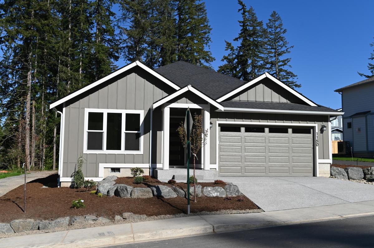 Gray suburban house with a two-car garage, landscaped front yard, and a paved driveway under a clear blue sky