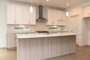 Bright modern kitchen with a large island, white upper cabinets, light wood lower cabinets, and a stainless steel range hood.