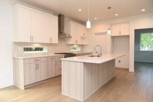 Bright modern kitchen with white upper cabinets, light wood lower cabinets, and a central island with a sink and pendant lights.