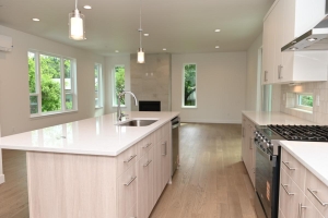 Bright, modern kitchen with a large central island, white countertops, and stainless steel appliances. Wide wood floor and ample natural light from multiple windows.