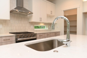 Modern kitchen with a stainless steel sink and curved faucet in a white island, visible gas range and range hood, and white upper cabinets. l
