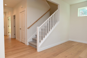 Light-filled hallway with a staircase on the right, white railing, and light wood floors.