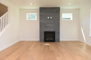 Bright living room with a tall gray slate fireplace wall centered between two small windows, and light hardwood floors.