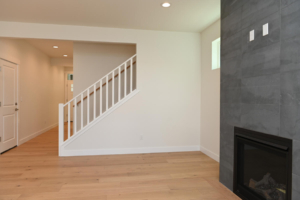 Living room with light wood flooring, white walls, a white staircase railing, and a gray tiled fireplace wall on the right.