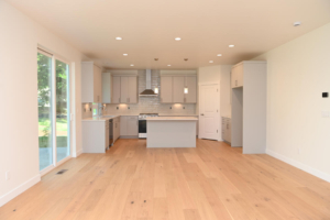 Open-plan kitchen with light gray cabinets, central island, stainless steel range hood, and sliding glass doors to the left.