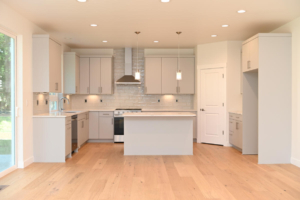 Modern gray kitchen with a central island, white backsplash, and stainless steel appliances; large sliding door to the left offering natural light.