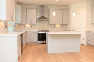 Bright and airy white kitchen with a large central island, light wood floors, stainless steel appliances, and pendant lights overhead.