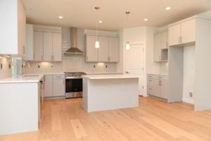 Bright modern kitchen with white cabinets, stainless-steel stove and range hood, central island, and light wood flooring.
