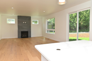 Bright living room with a dark slate fireplace, wide-plank hardwood floors, and a sliding glass door to a green yard.