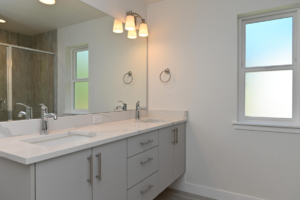 Double-sink bathroom vanity with white countertop and chrome faucets, under a large mirror in a bright room