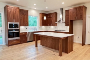 Modern kitchen with dark wood cabinets, white countertops, and a central island; stainless appliances and pendant lights above the island.