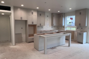 Spacious modern kitchen under construction with light gray cabinets and an island frame in progress.